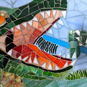 May include: Close-up of a mosaic artwork depicting a green alligator with an open mouth revealing sharp teeth. The alligator's eye is orange and the background is blue.