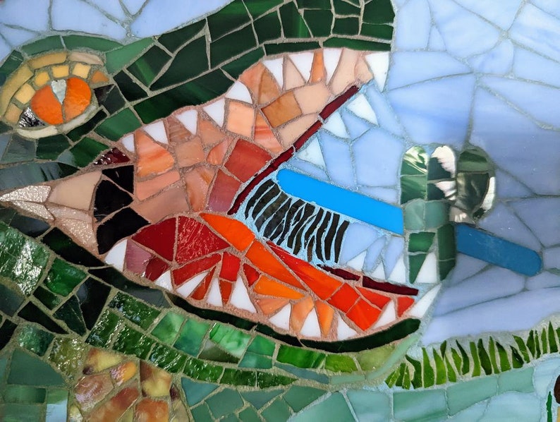 May include: Close-up of a mosaic artwork depicting a green alligator with an open mouth revealing sharp teeth. The alligator's eye is orange and the background is blue.