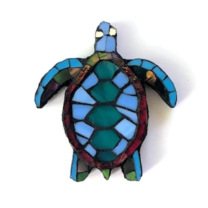 May include: A mosaic sea turtle figurine with a blue, green, and red color scheme. The turtle's shell is composed of various shades of blue and green glass pieces, with a red border. The flippers and head are blue.