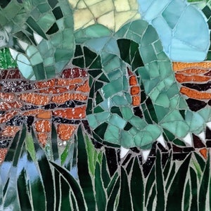 May include: A close-up of a mosaic artwork depicting a green leafy plant with a brown brick wall in the background. The mosaic is made of small, colorful glass tiles.