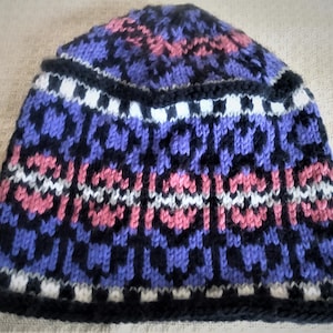 May include: A knitted hat with a black, purple, pink, and white geometric pattern.