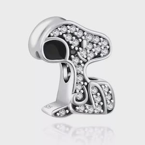 Könnte beinhalten: Ein silberner Charm in Form von Snoopy, mit Hut und schwarzem Auge. Der Charm ist mit zahlreichen klaren, funkelnden Kristallen besetzt. Auf der Basis des Charms steht "S925".