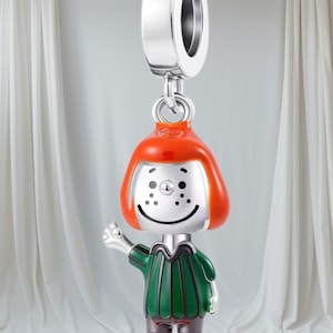 Könnte beinhalten: Ein silberner Charm-Anhänger mit einer Zeichentrickfigur mit orangefarbenem Haar, einem grün-braunen Outfit und einem ausgestreckten Arm. Der Charm-Anhänger ist für ein Armband oder eine Halskette konzipiert.