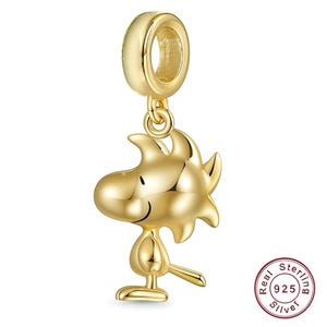 Könnte beinhalten: Ein goldfarbener Metallanhänger in Form der Figur Woodstock mit einer glatten, reflektierenden Oberfläche und einer runden Öse zur Befestigung. Ein kleiner runder Stempel in der Ecke trägt die Aufschrift Real Sterling 925 Silver.