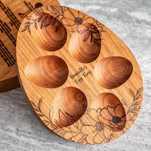 Peut inclure: Un plateau &agrave; &oelig;ufs en bois avec un motif floral et le texte "Danielle's Egg Tray" grav&eacute; sur le devant. Le plateau comporte six compartiments individuels pour contenir des &oelig;ufs.