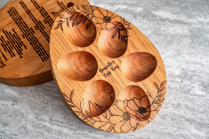Peut inclure: Un plateau &agrave; &oelig;ufs en bois avec un motif floral et le texte "Danielle's Egg Tray" grav&eacute; sur le devant. Le plateau comporte six compartiments individuels pour contenir des &oelig;ufs.