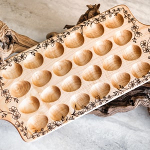 K&ouml;nnte beinhalten: Ein Holz-Eiertablett mit 20 einzelnen F&auml;chern, das mit einem floralen Muster verziert ist, das in das Holz gebrannt wurde. Das Tablett hat an jedem Ende einen Griff.