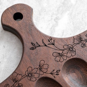 K&ouml;nnte beinhalten: Ein Holztablett mit einem floralen Design, das in die Oberfl&auml;che graviert ist. Das Tablett hat sechs einzelne Vertiefungen, perfekt zum Servieren von Vorspeisen oder Snacks.