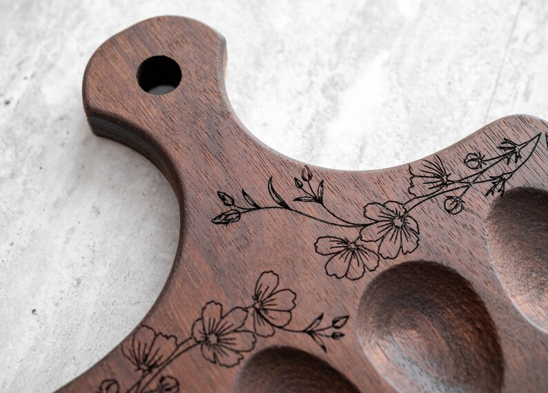 K&ouml;nnte beinhalten: Ein Holztablett mit einem floralen Design, das in die Oberfl&auml;che graviert ist. Das Tablett hat sechs einzelne Vertiefungen, perfekt zum Servieren von Vorspeisen oder Snacks.