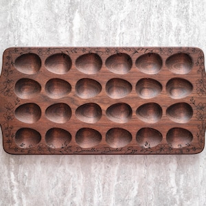 K&ouml;nnte beinhalten: Ein Eiertablett aus Holz mit 24 einzelnen Vertiefungen zum Aufbewahren von Eiern. Das Tablett ist mit einem floralen Muster am Rand graviert und die Worte "Douvillier Dusted Egg" sind auf der Unterseite graviert.