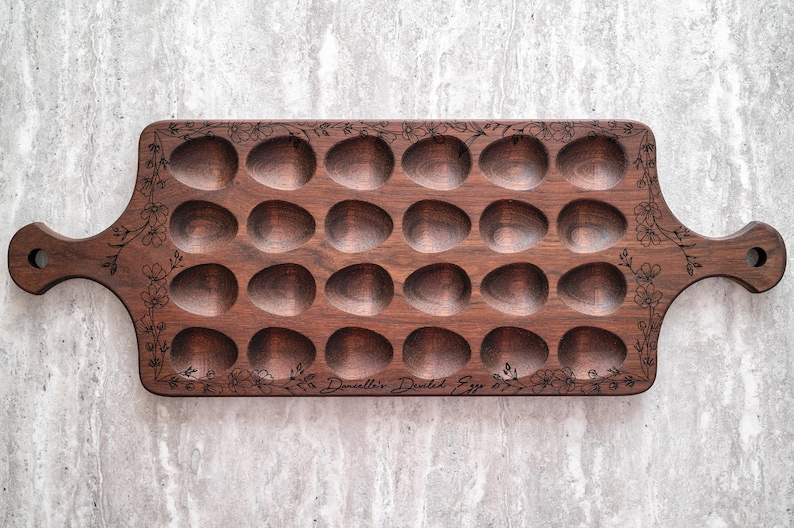 K&ouml;nnte beinhalten: Ein Eiertablett aus Holz mit 24 einzelnen Vertiefungen zum Aufbewahren von Eiern. Das Tablett ist mit einem floralen Muster am Rand graviert und die Worte "Douvillier Dusted Egg" sind auf der Unterseite graviert.