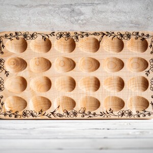 K&ouml;nnte beinhalten: Ein Eiertablett aus Holz mit floralem Design. Das Tablett hat 18 einzelne F&auml;cher zum Aufbewahren von Eiern. Es hat einen Griff auf einer Seite.