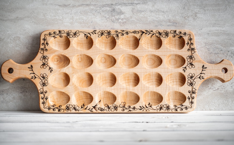 K&ouml;nnte beinhalten: Ein Eiertablett aus Holz mit floralem Design. Das Tablett hat 18 einzelne F&auml;cher zum Aufbewahren von Eiern. Es hat einen Griff auf einer Seite.