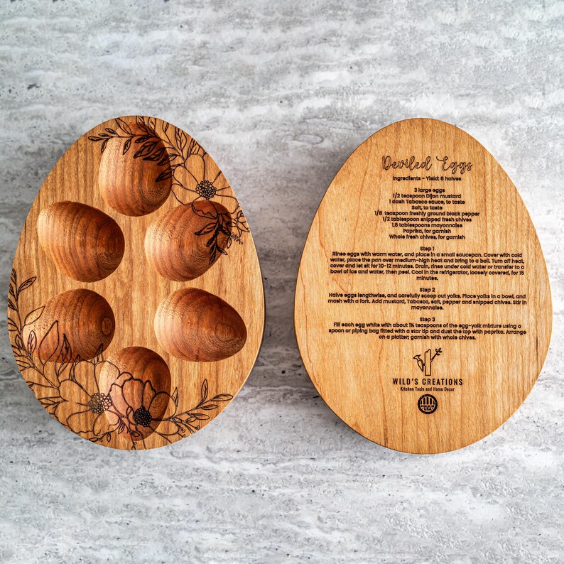 Peut inclure: Plateau de service en bois en forme d'&oelig;uf avec six indentations individuelles pour les &oelig;ufs &agrave; la diable. Le plateau est d&eacute;cor&eacute; de motifs floraux et les mots "Deviled Eggs" et "WILD'S CREATIONS" sont grav&eacute;s sur le plateau. Le plateau est en bois brun clair.