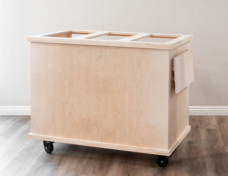 K&ouml;nnte beinhalten: Ein rollender Wagen aus Naturholz mit schlichtem Design. Der Wagen hat drei offene Regalb&ouml;den und ein kleines Seitenregal. Der Wagen ist aus unbehandeltem Holz und hat schwarze R&auml;der.