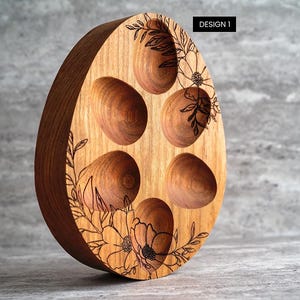 Peut inclure: Porte-&oelig;ufs en bois en forme d'&oelig;uf avec six compartiments individuels pour contenir des &oelig;ufs. Le porte-&oelig;uf est d&eacute;cor&eacute; d'un motif floral et du texte "DESIGN 1".