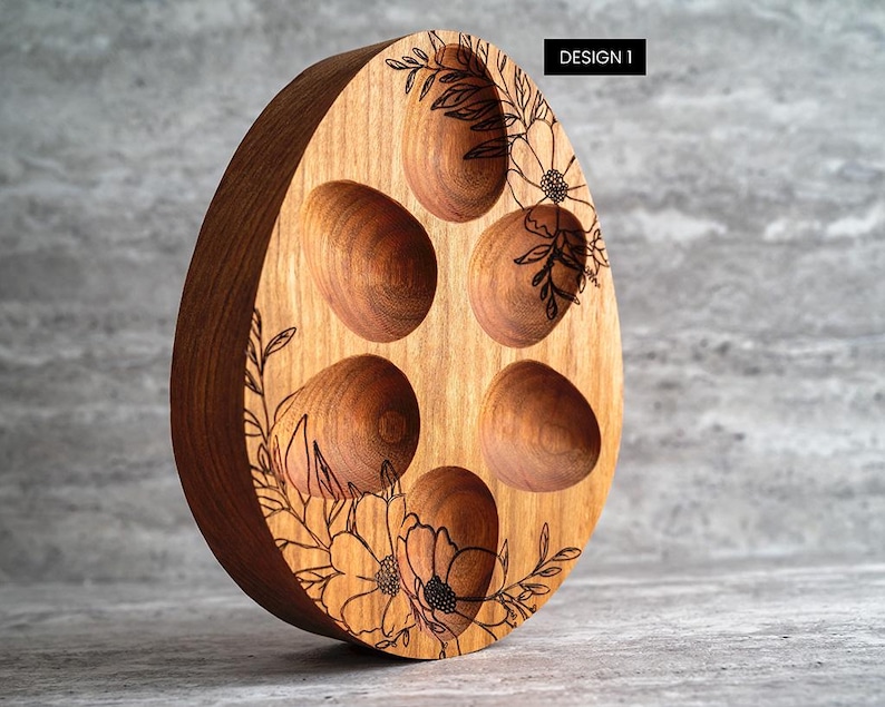 Peut inclure: Porte-&oelig;ufs en bois en forme d'&oelig;uf avec six compartiments individuels pour contenir des &oelig;ufs. Le porte-&oelig;uf est d&eacute;cor&eacute; d'un motif floral et du texte "DESIGN 1".