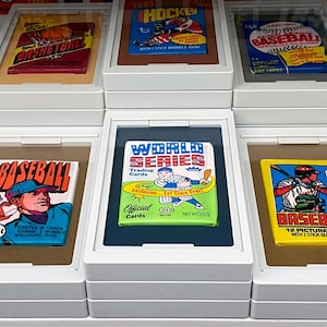 May include: A collection of vintage baseball trading cards in white display cases. The cards feature colorful illustrations of baseball players and the text "Baseball", "World Series", "Hockey", and "Major League".