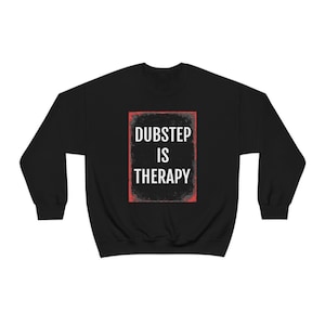May include: Black sweatshirt featuring the phrase "DUBSTEP IS THERAPY" in white, within a red and grey rectangular frame. A comfortable, casual garment, ideal for everyday wear.