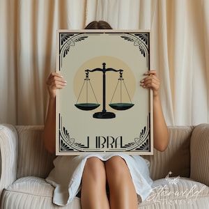 May include: A framed Libra zodiac sign art print. The artwork features a black scale design on a cream background with a yellow circle. The word "LIBRA" is printed in black at the bottom. The frame has a decorative black border.