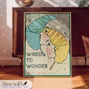 Könnte beinhalten: Ein gerahmter Kunstdruck im Vintage-Stil. Das Kunstwerk zeigt drei stilisierte weibliche Profile in Blau, Rosa und Gelb mit den Worten "WIRED TO WONDER". Der Druck enthält auch die Daten "MAY 21 - JUNE 20" auf cremefarbenem Hintergrund.