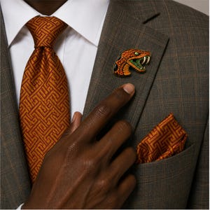 May include: A brown plaid blazer with a white dress shirt, a burnt orange tie featuring a geometric maze pattern, a matching pocket square, and a gold-toned enamel lapel pin shaped like a snake head with orange scales and green accents.
