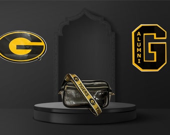 May include: A clear plastic crossbody bag with a black zipper and a black and yellow strap that says "G TIGERS G TIGERS". The bag is sitting on a black platform in front of a black wall with two yellow and black "G" logos.