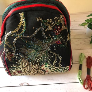 May include: A black sequined backpack with a peacock design. The backpack has red and green trim and a zipper closure.