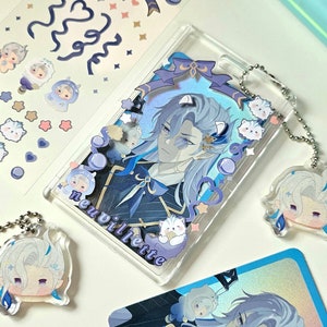 May include: A clear phone case with a blue and white anime character design. The case has a silver chain attached to it. The character's name, "neuvillette", is written on the case. There are also several small, white, cartoon animal stickers on the case.