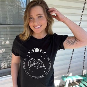 May include: Black t-shirt with a white graphic of a bat flying in front of a crescent moon and the text "Protect Our Nocturnal Pollinators".