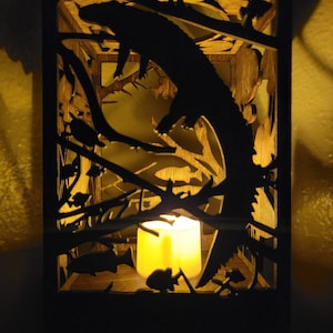 May include: A wooden lantern with a silhouette of a fish jumping out of the water. The lantern has a candle inside, casting a warm glow.