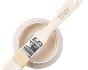 May include: A round container filled with light beige paint and a wooden paintbrush resting on top. The brush handle features the text FUSION MINERAL PAINT and the metal ferrule is clearly marked with the measurement 1 inch or 25.4mm.