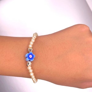May include: A white pearl bracelet with a blue and white flower charm and gold heart charms.