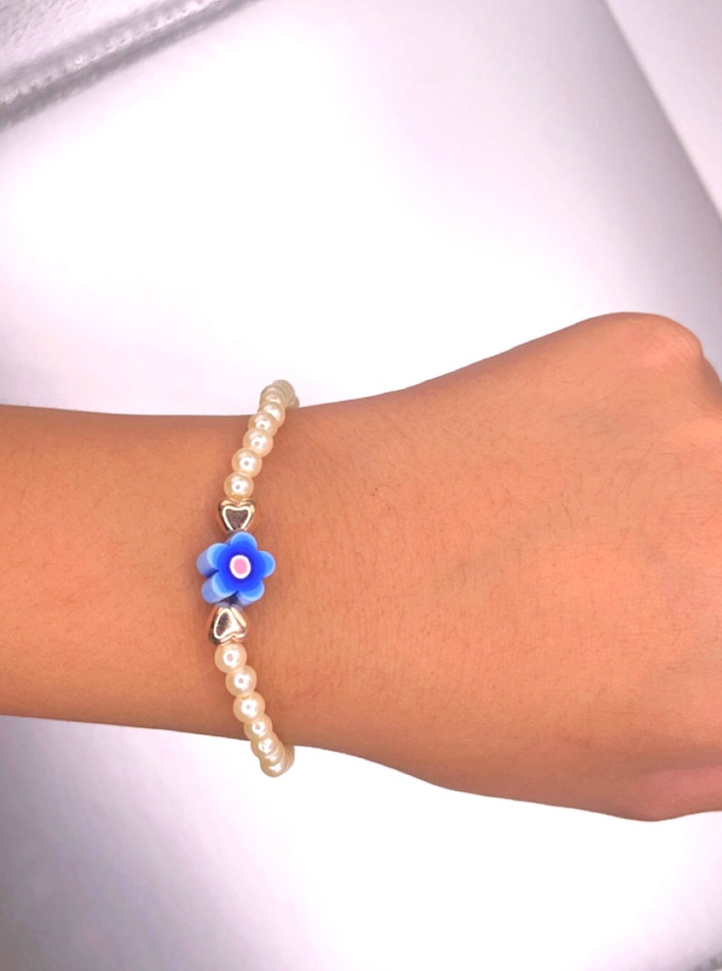 May include: A white pearl bracelet with a blue and white flower charm and gold heart charms.
