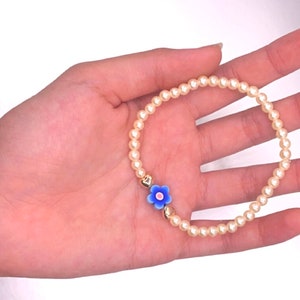 May include: A delicate bracelet made of white pearls with a blue and white flower charm.