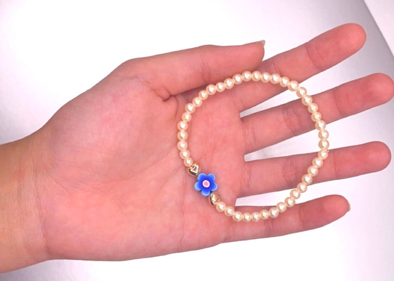 May include: A delicate bracelet made of white pearls with a blue and white flower charm.
