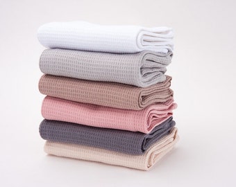 May include: A stack of six waffle weave towels in various colors, including white, gray, brown, pink, and dark gray. The towels are folded and stacked on top of each other.