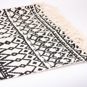 May include: Black and white geometric patterned rug with fringe on the edges.