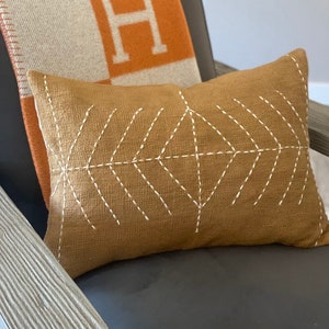 May include: A brown throw pillow with a white geometric pattern on a gray chair. The pillow is made of a textured fabric and has a subtle sheen.