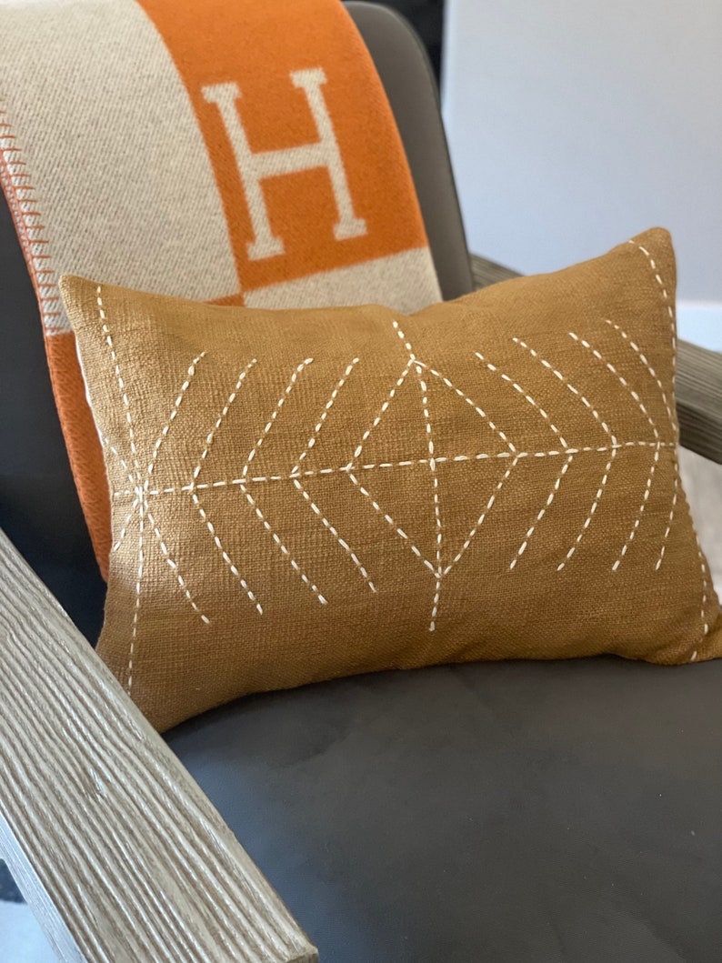 May include: A brown throw pillow with a white geometric pattern on a gray chair. The pillow is made of a textured fabric and has a subtle sheen.