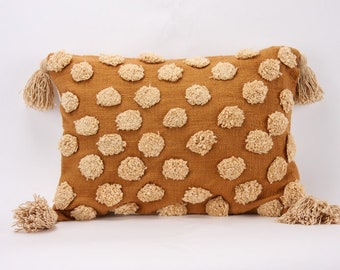 May include: A mustard yellow throw pillow with a textured pattern of beige circles. The pillow has fringe tassels on each corner.
