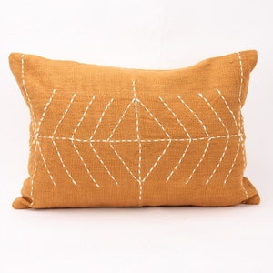 May include: A mustard yellow throw pillow with a white geometric design stitched on the front.