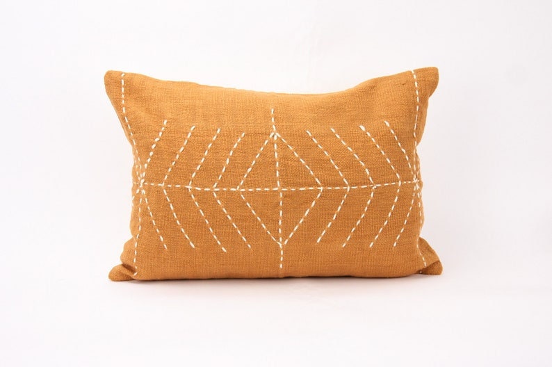 May include: A mustard yellow throw pillow with a white geometric design stitched on the front.