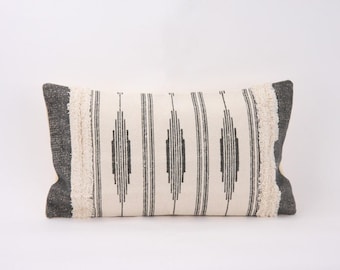 May include: A white and black patterned lumbar pillow with a fringe border. The pillow has a geometric design with black lines and diamonds on a white background.