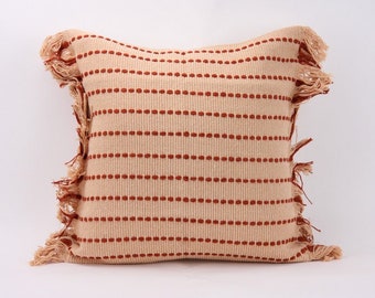 May include: A square throw pillow with a cream colored fabric and red stripes. The pillow has a fringe border.