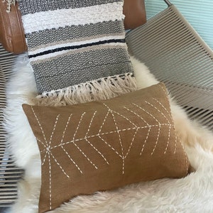 May include: A brown throw pillow with white stitching in a geometric pattern. The pillow is sitting on a white faux fur throw.
