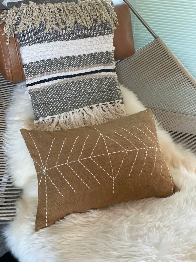May include: A brown throw pillow with white stitching in a geometric pattern. The pillow is sitting on a white faux fur throw.