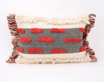 May include: A rectangular throw pillow with a white background and a black and red geometric pattern. The pillow has a fringe border.