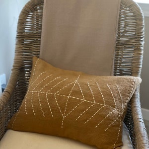 May include: A wicker chair with a beige throw blanket and a brown throw pillow with white stitching in a geometric pattern.