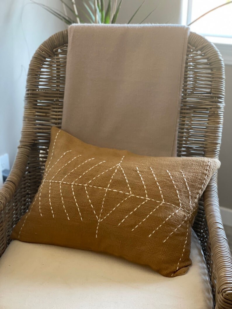 May include: A wicker chair with a beige throw blanket and a brown throw pillow with white stitching in a geometric pattern.
